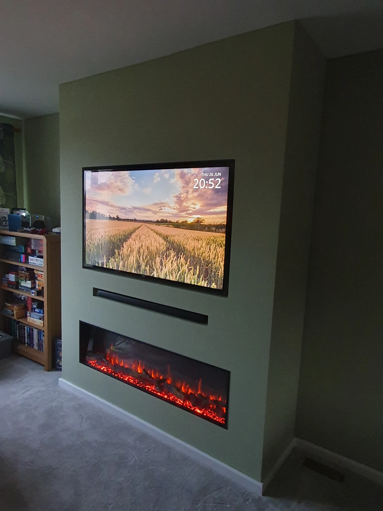 Front view of finished sage green media wall with TV displaying a wheat field, soundbar recess and wide linear flame fire